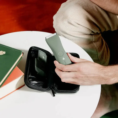 person't hand holding the Meridian body hair trimmer over the travel case